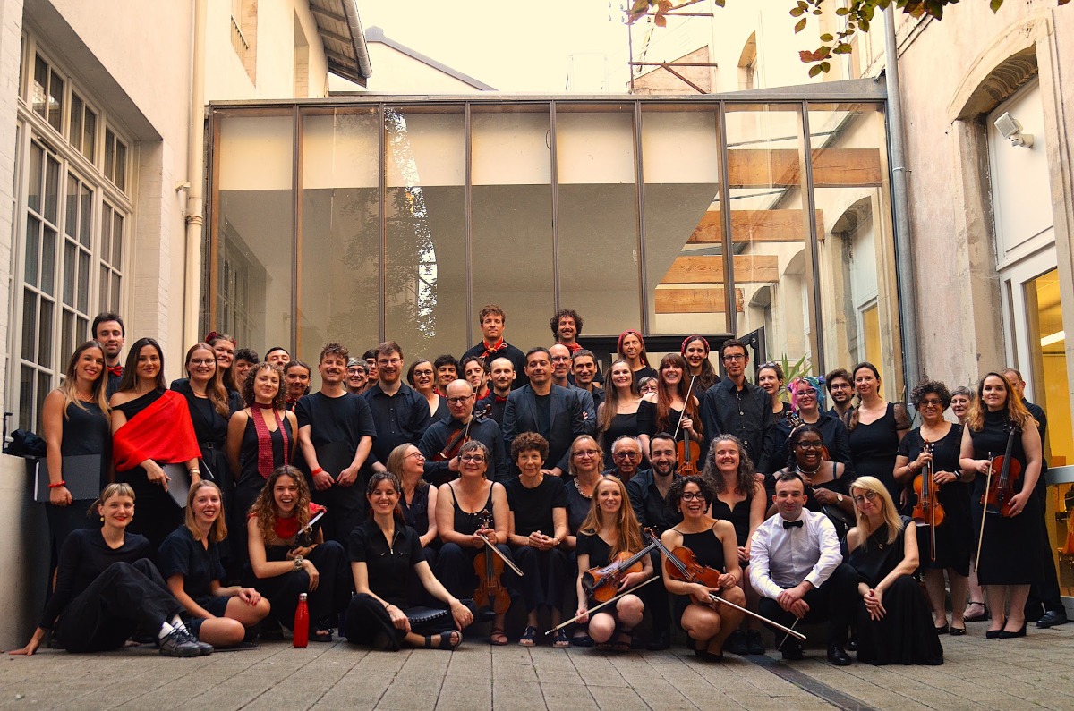 Les musiciens de l'Ensemble Arcovivo et les choristes invités, tout en noir, réunis pour la photo de groupe dans une cour vitrée, instruments à la main.